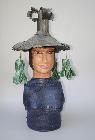 Ceramic sculpture of Village Deity with bak choi vegetables hanging from hat